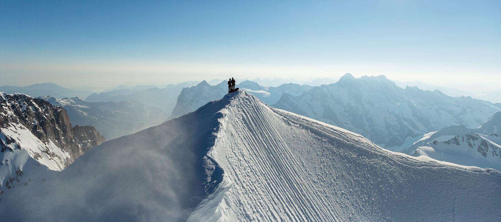 Aerial landscape view mountain summit Switzerland two successful climbers on snow covered Peak in sunlight travel tourism Europe