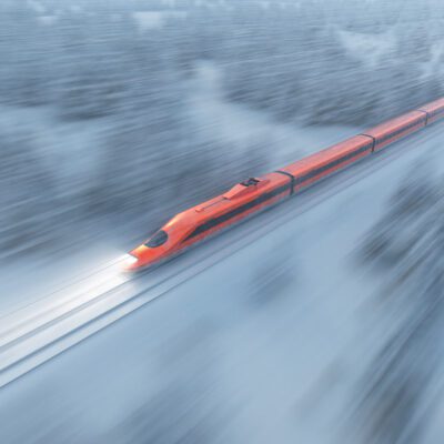 A high speed bullet train zooms through a snow-covered forest during winter, with snowflakes falling heavily. High-speed rail travel in a scenic winter landscape.